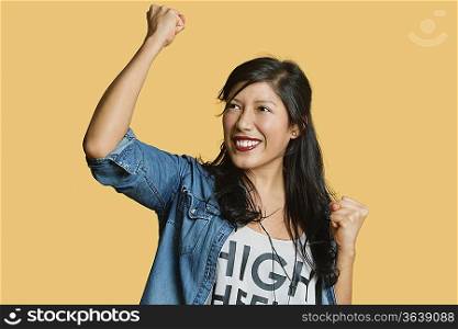 Excited young woman with raised fist while looking away over colored background