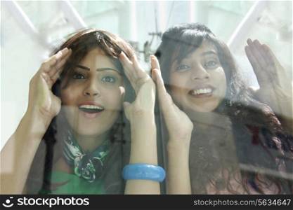 Excited young women peeking through window