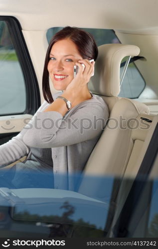 Executive attractive female manager sitting in car backseat calling phone
