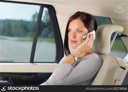Executive attractive female manager sitting in car backseat calling phone