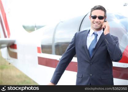 Executive chatting on the phone in front of a small aeroplane