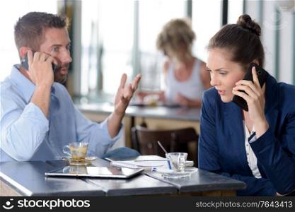 executive couple in a cafe both talking on smartphones