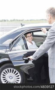 Executive holding car door for smiling colleague against sky