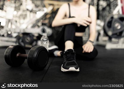 exercise concept The female with dark tone of outfits resting herself on the black carpet floor after playing on the dumbbell beside her.