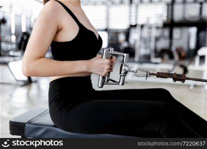 exercise concept The lady wearing sport top, tight pants and black sneakers sitting and concentrating on pulling a flexible rope of seat roll machine.