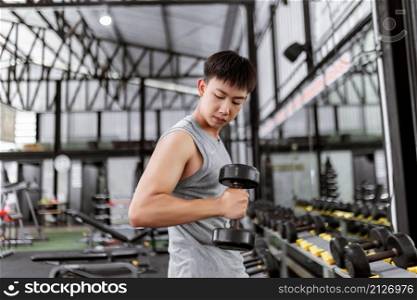 exercise concept The sweaty guy in grey top looking down and doing hammer curl posture of dumbbell with his right arm.