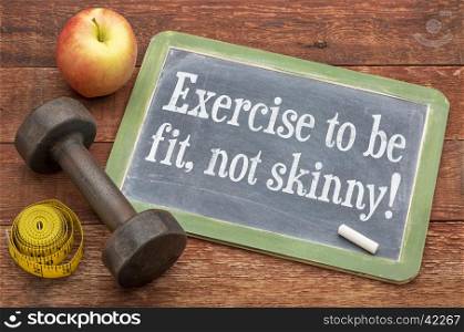 Exercise to be fit, not skinny! Fitness concept on a slate blackboard against weathered red painted barn wood with a dumbbell, apple and tape measure