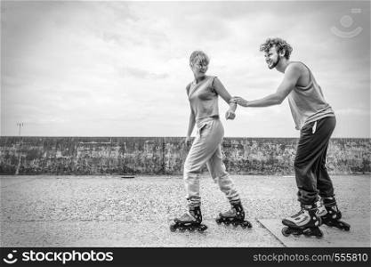 Exercising and competition in sport. Healthy lifestyle and wellbeing. Summertime hobby. Young people race together on rollerblades having fun black and white.. Two people race together riding rollerblades.