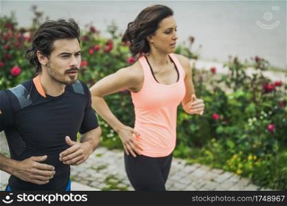 Exercising by the river with personal trainer. Fit Young Couple Jogging Outdoors 