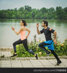 Exercising by the river with personal trainer. Fit Young Couple Jogging Outdoors 