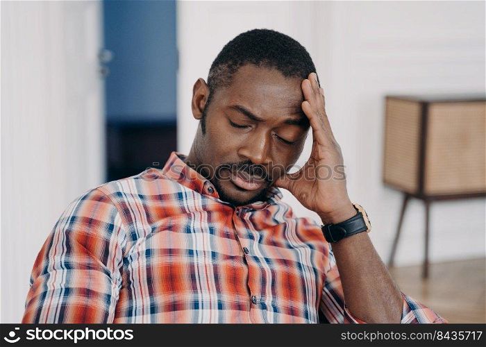 Exhausted african american man touches head suffer from headache or migraine, tired upset black guy with closed eyes feel fatigue due to lack of sleep, problems at work, life crisis.. Tired frustrated african american man suffer from headache or migraine. Fatigue, stress, life crisis