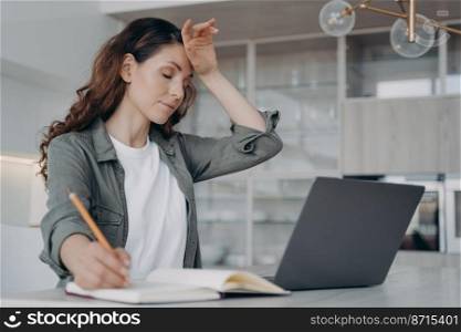 Exhausted female student touching her forehead, tired of monotony studying at laptop at home. Weary woman working remotely online on computer feeling fatigue, lack of energy. Remote work, education.. Tired female working or studying online at laptop. Fatigue, lack of energy. Remote work, education