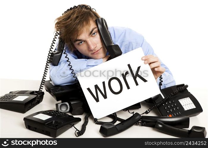 Exhausted man full of work, sitting with a bunch of phones over him and holding a cardboard with the word Work.