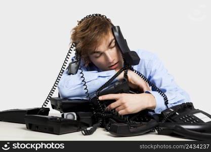 Exhausted man sitting with a bunch of phones over him