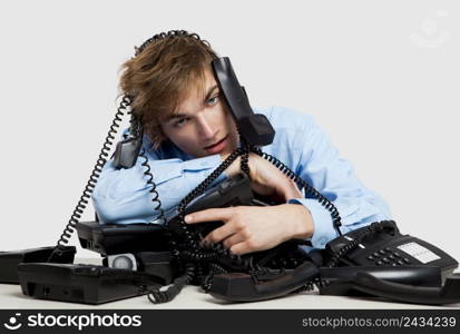 Exhausted man sitting with a bunch of phones over him