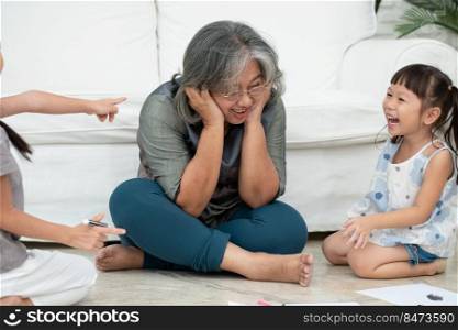 Exhausted old elderly grandmother sit on floor in living room and feel unwell tired from little children running and playing loud, suffer from headache, female nanny feels exhausted by noisy kids