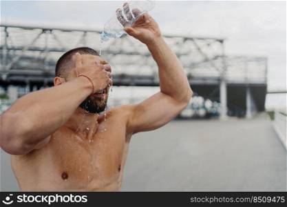 Exhausted sportsman splashes fresh cold water over head, tries to refresh after hard exercising outdoor, poses shirtless, has strong muscles and perfect body shape. Hydration and sport concept