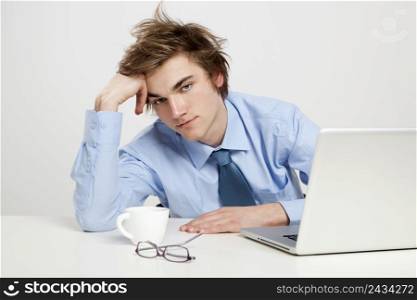 Exhausted young man in the office with the laptop on his front