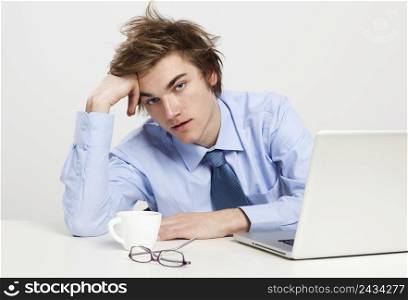 Exhausted young man in the office with the laptop on his front