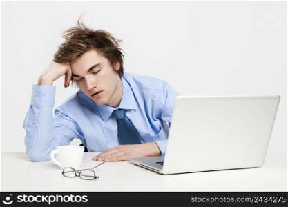 Exhausted young man in the office with the laptop on his front and sleeping