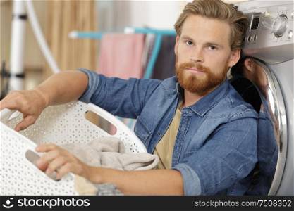 exhausted young man with laundry basket sitting on floor
