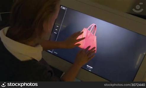 Exhibition visitor is viewing 3D model of red bag on big touch screen set on TechTrendsExpo.