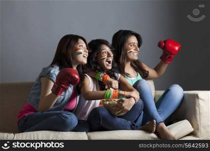Exhilarated young female friends watching boxing match together at home