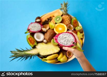 exotic food, summer and healthy eating concept - close up of hand holding half of dragon fruit over blue background. hand holding half of dragon fruit over blue