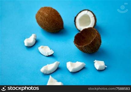 exotic fruits, eating and food concept - whole and cracked coconut on blue background. whole and cracked coconut on blue background