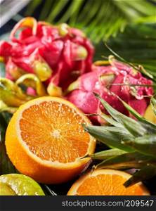 Exotic tropical background with pitahaya, the half of orange in a water drops on a large palm leaf. Dieting natural vegetarian concept. Close-up. Close-up of exotic background from fresh ripe tropical fruits dragon fruits, pitahaya, the half of orange, pineapple leaf.