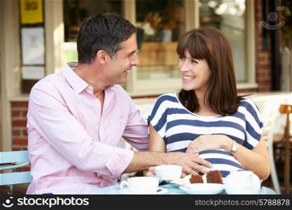 Expectant couple sitting outside cafe
