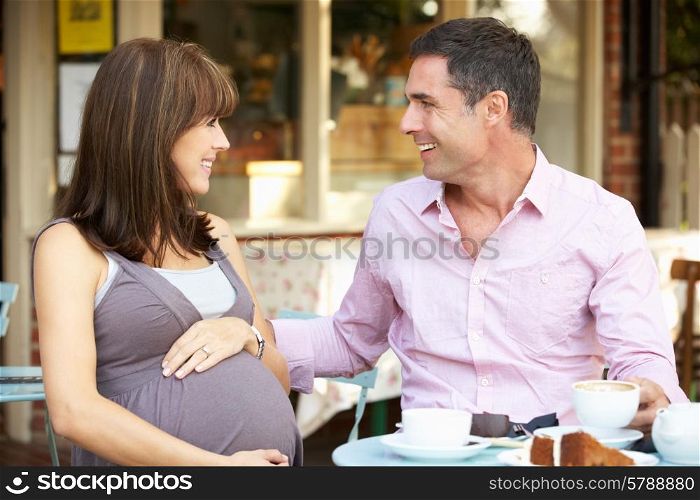Expectant couple sitting outside cafe
