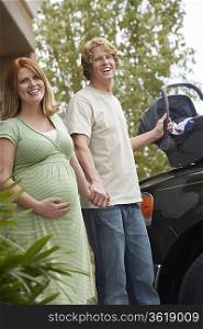 Expectant couple with baby carrier by car, portrait