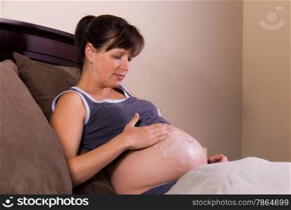 Expecting mother putting moisturizing lotion on her tummy