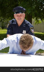 Experienced, mature policeman looking at the camera as he pats down a suspect.