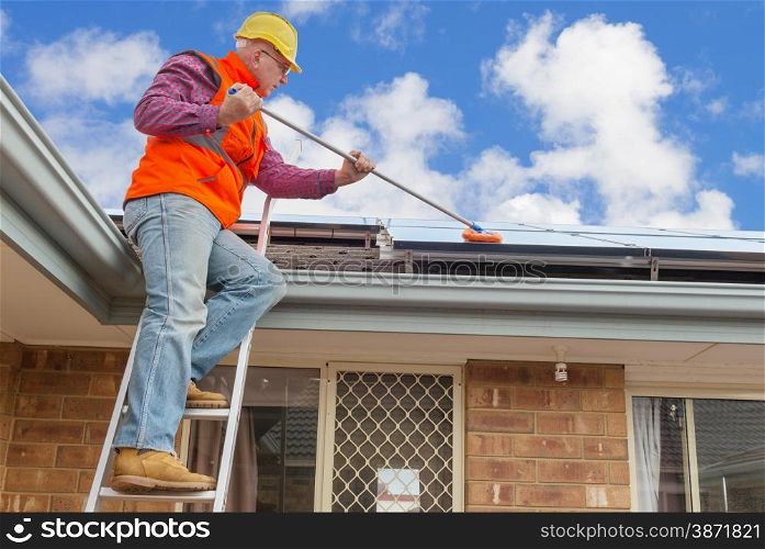 experienced worker cleaning solar panels on house roof