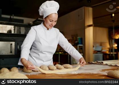 Experienced young woman baker working in bakery, forming baguettes from raw dough. Bakery shop and manufactory concept. Young woman baker working in bakery, forming baguettes from raw dough
