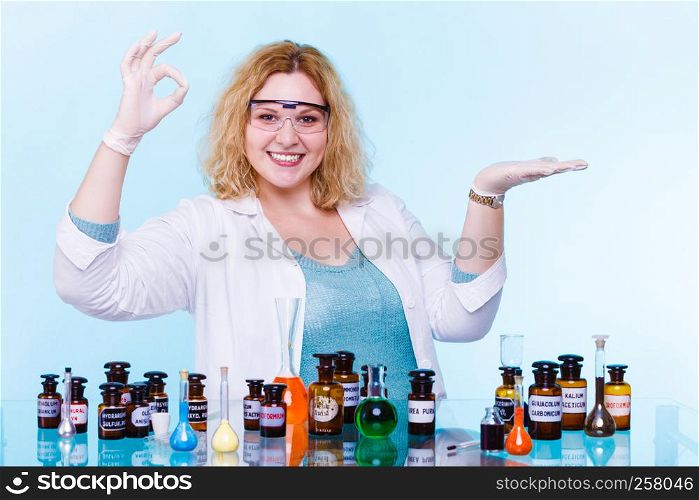 Experiments in laboratory. Happy chemist woman or scientific researcher with chemical test flask making ok hand sign holding open palm on blue