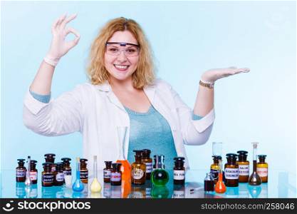 Experiments in laboratory. Happy chemist woman or scientific researcher with chemical test flask making ok hand sign holding open palm on blue