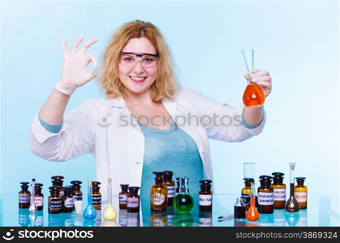 Experiments in laboratory. Happy chemist woman or student girl scientific researcher with chemical glassware test flask making ok hand sign on blue