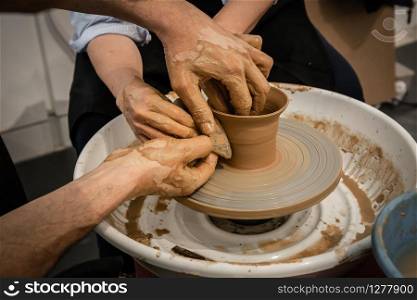 Expert potter teach a woman to work on potter wheel. Closeup of dirty hands