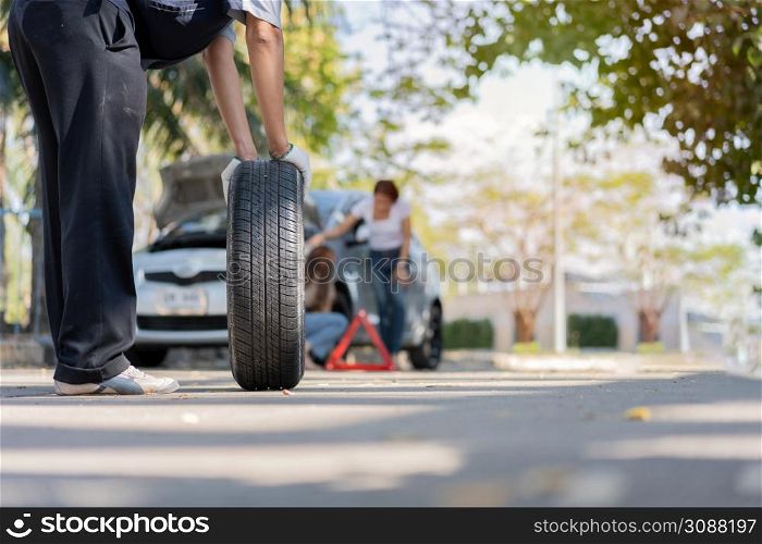 Expertise mechanic man in uniform holding a tire for help a woman for changing car wheel on the highway, car service, repair, maintenance concept.