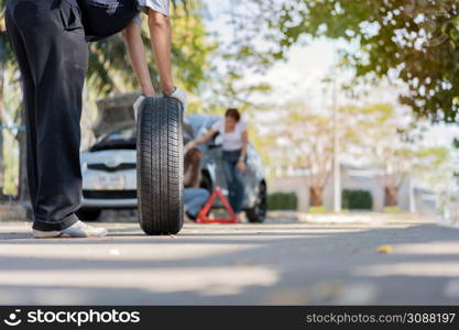 Expertise mechanic man in uniform holding a tire for help a woman for changing car wheel on the highway, car service, repair, maintenance concept.