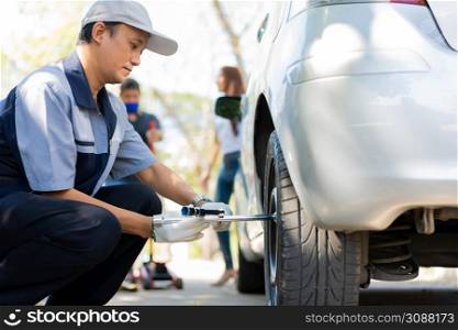 Expertise mechanic man in uniform using force trying to unscrew the wheel bolts nuts and help a woman for changing car wheel on the highway, car service, repair, maintenance concept.