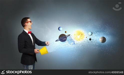 Exploring the universe. Young man splashing from bucket planets of space spinning around