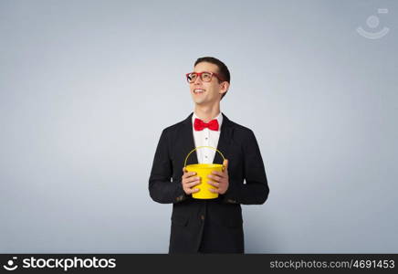 Express your creative individuality. Young man in jacket and red glasses with yellow bucket in hands