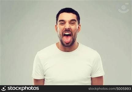 expression, rudeness and people concept - man showing his tongue over gray background. man showing his tongue over gray background