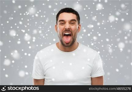 expression, rudeness, winter, christmas and people concept - man showing his tongue over snow on gray background