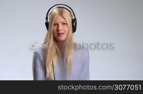 Expressive girl in headphones listening to rhythmic music on the radio over white background. Cheerful young woman enjoying the music, making dance moves and singing along.