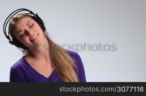 Expressive teenage girl in headphones having fun while listening to music on white background. Emotional cheerful brunette woman with earphones enjoying favorite song, making funny facial expressions, singing along and playfully looking at camera.